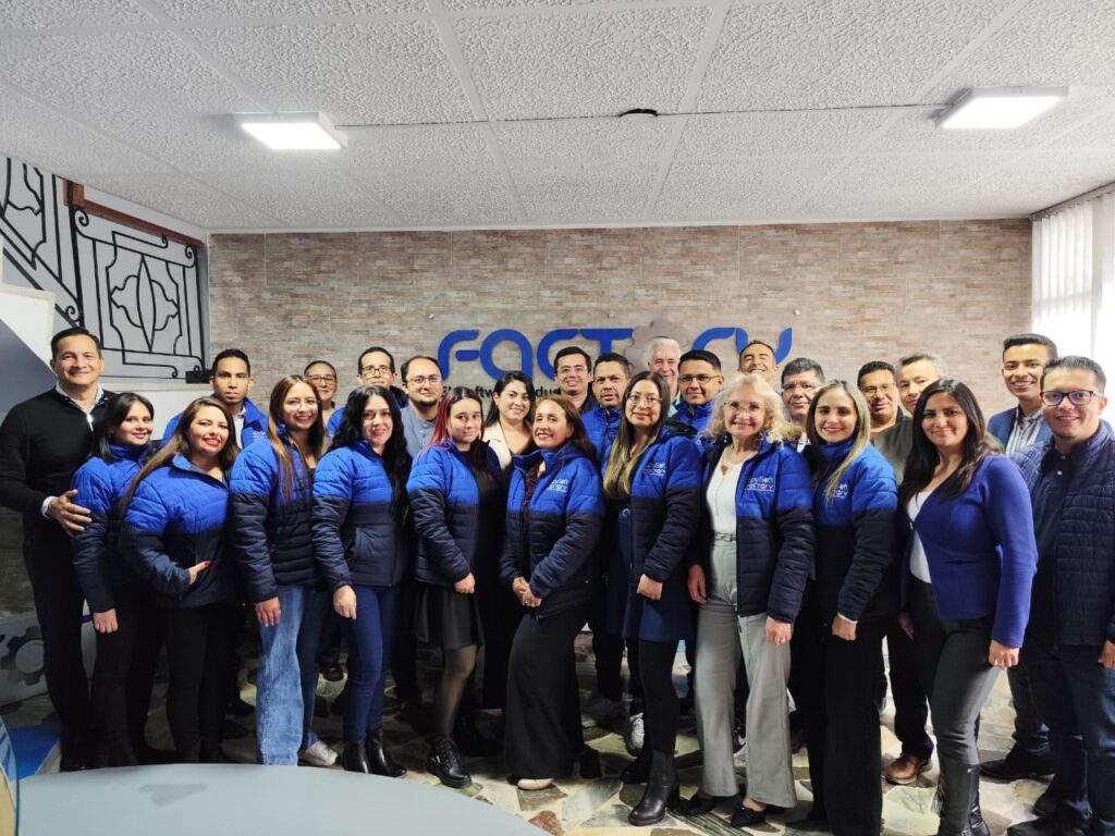 Equipo de Factory posando frente al logotipo corporativo, representando la unidad y el talento humano de todas las áreas de la compañía